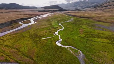 Dolambaçlı, dolambaçlı plato. Yeşil çimlerde, yemyeşil yemyeşil çayırlarda ve tepelerde dereler var. İnsansız hava aracının panoramik görüntüsü.