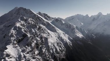 Hava görüntüsü. Güneşli bir günde dağlık bölgenin karlı zirvelerini gösteren görkemli dağ sıralarının nefes kesici kuş bakışı görüntüsü. Panning Hareketi. Nazikçe hareket ederek doğal güzellikleri ortaya çıkarıyor..