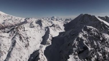 Hava görüntüsü. Güneşli bir günde dağlık bölgenin karlı zirvelerini gösteren görkemli dağ sıralarının nefes kesici kuş bakışı görüntüsü. Panning Hareketi. Nazikçe hareket ederek doğal güzellikleri ortaya çıkarıyor..