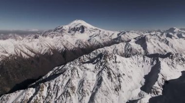 Hava görüntüsü. Güneşli bir günde dağlık bölgenin karlı zirvelerini gösteren görkemli dağ sıralarının nefes kesici kuş bakışı görüntüsü. Panning Hareketi. Nazikçe hareket ederek doğal güzellikleri ortaya çıkarıyor..