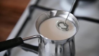 Metal bir kahve demliğinde gaz sobasında kaynayan bir süt. Elle tutulan köpük sütü köpürür. Ev yapımı kahve.