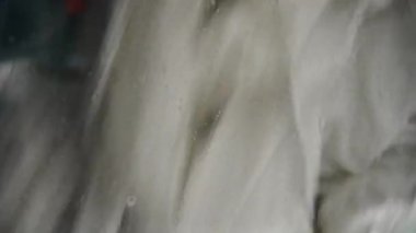 Bir zamanlar çamaşır makinesinde yıkanan, eski, sarı gri çamaşırların yakın çekimi. Deterjan köpükleri camdan aşağı damlıyor.