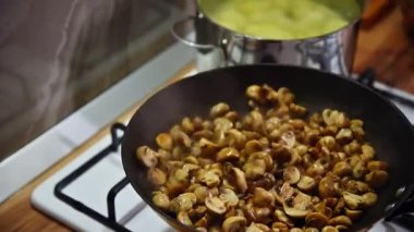 Mutfaktaki gaz sobasında tavada kızartılan küçük altın mantarların yavaş çekimleri. Mantarlar tavaya atılır ve karıştırılır..