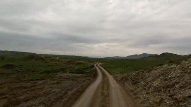 Bulutlu bir gün, toprak yolda hızlı sürüş. Arabaların ön camından görüntü. Hareket bulanıklığı olmayan bir aksiyon kamerasıyla çekilmiş.
