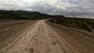 Bulutlu bir gün, toprak yolda hızlı sürüş. Arabaların ön camından görüntü. Hareket bulanıklığı olmayan bir aksiyon kamerasıyla çekilmiş.