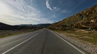 Dolambaçlı bir asfalt dağ yolunda araba sürüyorum. Dağlık arazide asfalt bir yol. Birinci şahıs görüntüsü, hareket bulanıklığı olmayan bir aksiyon kamerasıyla çekildi