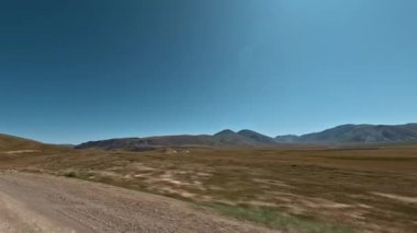 Bir dağ manzarasının yanından hızla geçen bir off-road aracının görüntüsü. Aksiyon kamerasıyla çekilmiş.