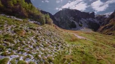 Bir FPV insansız hava aracının hava görüntüsü güneşli bir yaz gününde nehir boyunca bir geçitten bir şelaleye uçuyor.