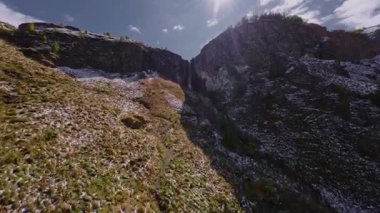 Bir FPV insansız hava aracının hava görüntüsü güneşli bir yaz gününde nehir boyunca bir geçitten bir şelaleye uçuyor.