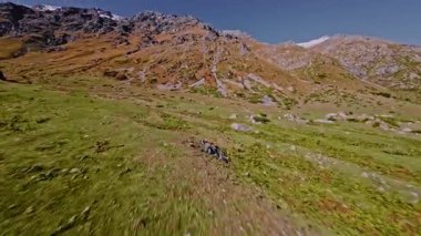 Dağlardaki tepelerin üzerinden alçak uçuş. Güneşli bir günde, bir FPV insansız hava aracının havadan birinci şahıs görüntüsü.