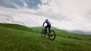 Dağ yamacında yeşil çimenler üzerinde bisiklet süren bisikletçinin yan görüntüsü. Bisikletli profesyonel bisikletçi, koruyucu kask takıyor ve bisiklet üzerinde aşırı serbest çalışma yapıyor..
