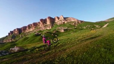 Miğferli ve maskeli genç bir sporcu gün batımında arka tekerlere binip pedal çeviriyor. Fpv insansız hava aracında hava görüntüsü