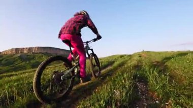 Miğferli ve maskeli genç bir sporcu gün batımında arka tekerlere binip pedal çeviriyor. Fpv insansız hava aracında hava görüntüsü.