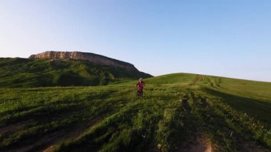 Miğferli ve maskeli genç bir sporcu gün batımında arka tekerlere binip pedal çeviriyor. Fpv insansız hava aracında hava görüntüsü.