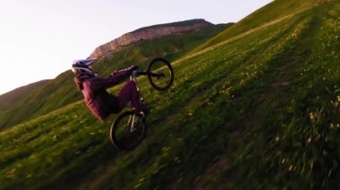 Yakın plan genç erkek binici, dağlarda yavaş çekimde bisikletiyle bisiklete biniyor. Fpv insansız hava aracının epik kaya dağları görüntüsü.