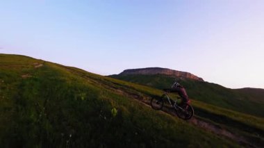 Hava görüntüsü fpv. Bisikletçi, arka planda kayalar ve destansı dağlarla dağda bisiklet sürüyor. Gün batımında