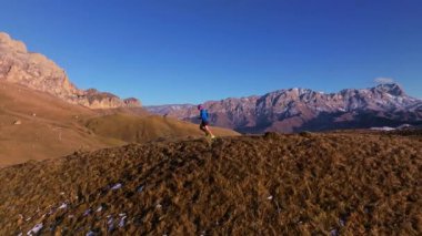 Spor görüntüleri, sonbaharda dağ sırtında koşan genç bir adamın karlı dağların büyüleyici manzarası. Dağlarda dayanıklılık eğitimi..