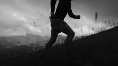 Siyah beyaz monokrom video. Yüksek kontrastlı. Genç sporcu dağ manzarası ve bulutların zeminine karşı yüksek dağlara tırmanıyor..