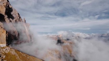 Hava sinemasının hava manzarası alçak bulutların arasında ve yanında destansı bir dağ arazisindeki kaya oluşumlarında dinleniyor..