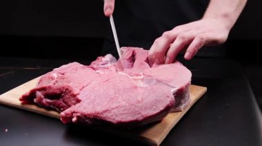 Bir adam kızarmadan önce büyük bir biftek hazırlar. Terbiye etmek için kesim yapıyor.
