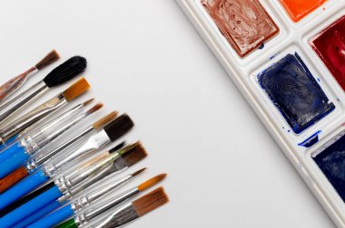 Fotokopi alanı olan beyaz bir zemin üzerinde suluboya boya ve fırça seti. Arkaplan sanatı ve resim tasarımı.