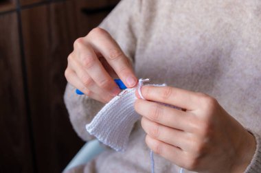 Beyaz bir tekstil ören bir kadın, mavi bir kanca kullanıyor, ahşap arka planı olan kapalı bir yerde oturuyor ve çalışma alanını geliştiren yumuşak doğal ışık var.