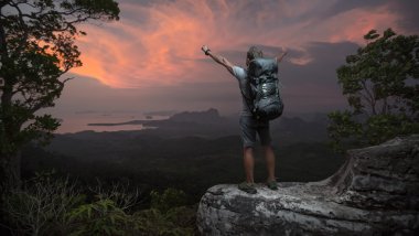 bir dağın tepesinde uzun yürüyüşe çıkan kimse