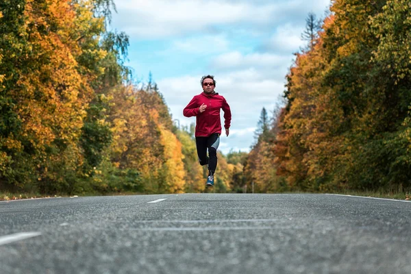 Muž běží dolů na silnici, v lese — Stock fotografie