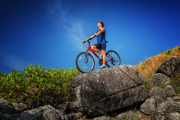 Homem de pé com uma bicicleta na rocha — Fotografia de Stock