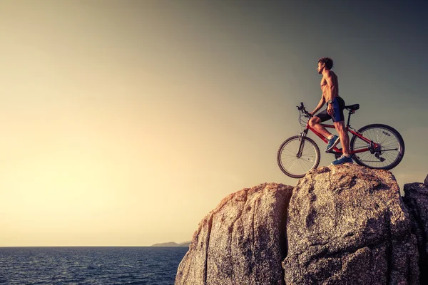 Homem de pé com uma bicicleta na rocha — Fotografia de Stock