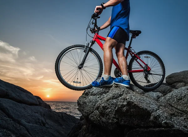 Homem de pé com uma bicicleta na rocha — Fotografia de Stock