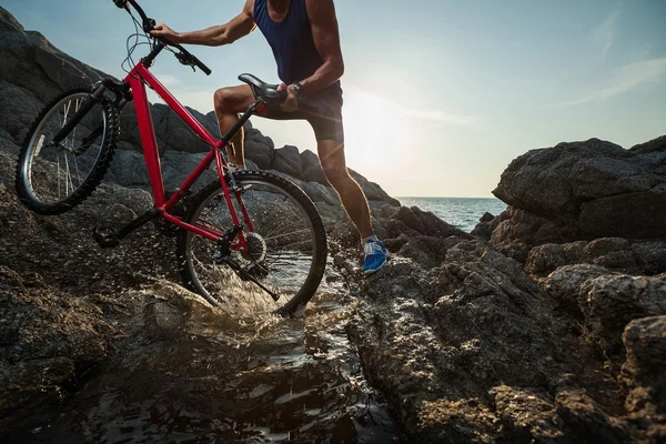 Homme portant un vélo à travers l'eau — Photo