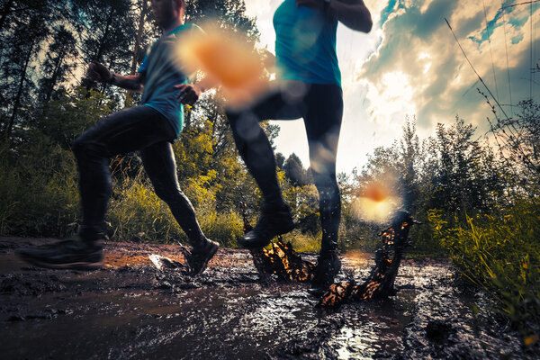 Two athletes running through the dirty puddle