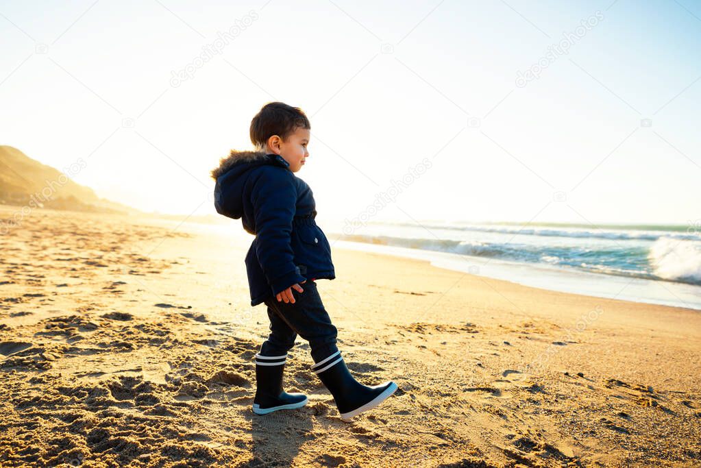 Little boy walking on beach at sunset, winter season
