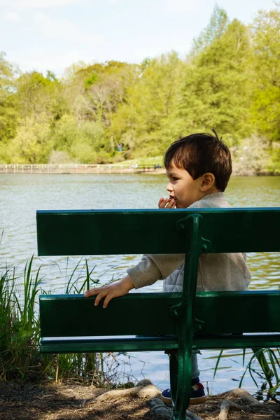 Liten pojke äter en kaka på bänk på stranden — Stockfoto