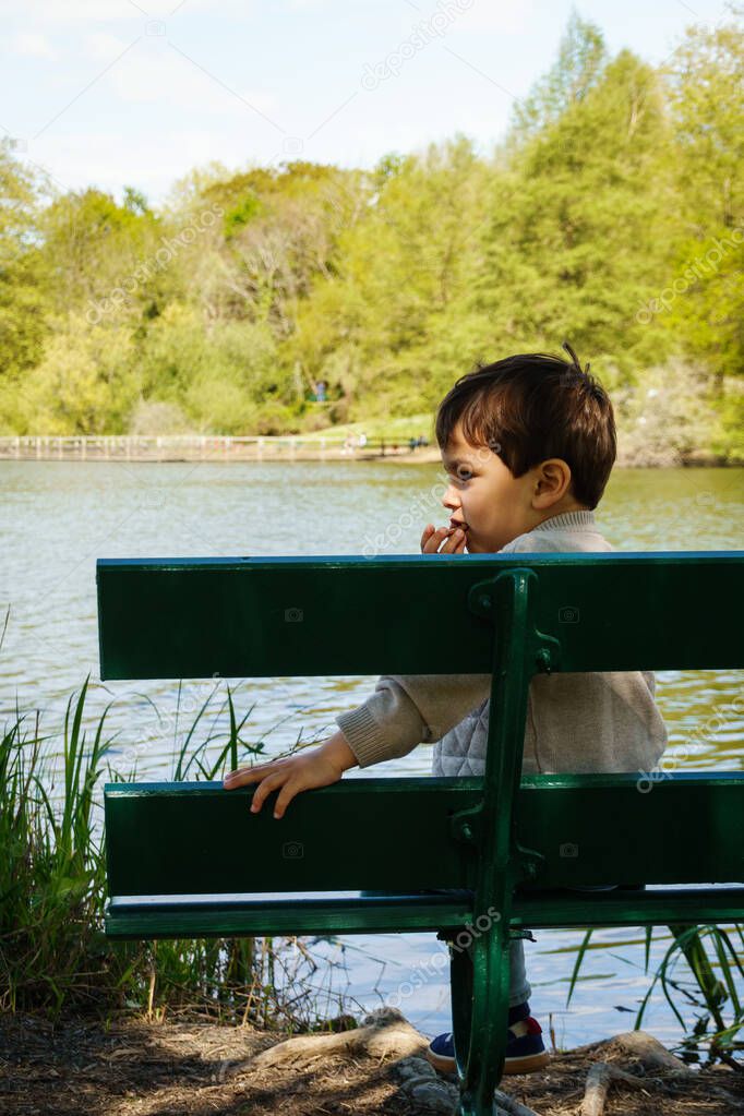 Little boy eating a biscuit on bench on lakeshore