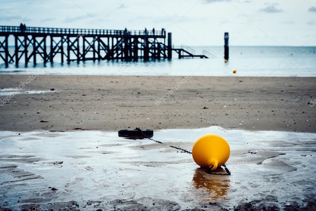 Orange buoy on a beach, pier in the background