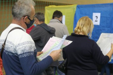 ODESSA, UKRAINE -25.10.2020 - Ukrayna 'da seçimler. COVID-19 Coronavirus salgını sırasında yerel meclis üyelerinin seçim platformu. Oy pusulalarıyla maske ve eldiven takan insanlar