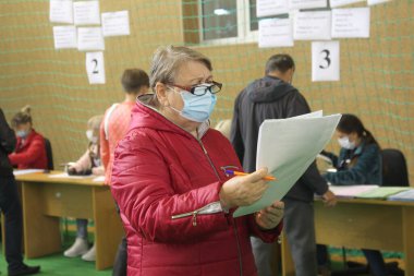ODESSA, UKRAINE -25.10.2020 - Ukrayna 'da seçimler. COVID-19 Coronavirus salgını sırasında yerel meclis üyelerinin seçim platformu. Oy pusulalarıyla maske ve eldiven takan insanlar