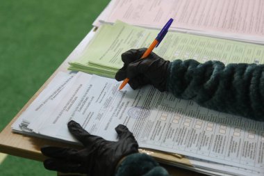 ODESSA, UKRAINE -25.10.2020 - Ukrayna 'da seçimler. COVID-19 Coronavirus salgını sırasında yerel meclis üyelerinin seçim platformu. Oy pusulalarıyla maske ve eldiven takan insanlar