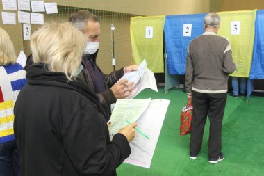 ODESSA, UKRAINE -25.10.2020 - Ukrayna 'da seçimler. COVID-19 Coronavirus salgını sırasında yerel meclis üyelerinin seçim platformu. Oy pusulalarıyla maske ve eldiven takan insanlar