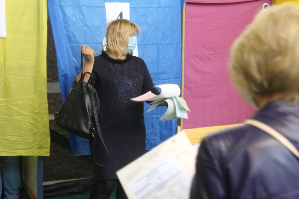 ОДЕССА, Украина -25.10.2020 - Выборы в Украине. Избирательная платформа для выборов местных советников во время пандемии коронавируса COVID-19. Люди в масках и перчатках с бюллетенями для голосования