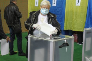 ODESSA, UKRAINE -25.10.2020 - Elections in Ukraine. Electoral platform for elections of local councilors during the COVID-19 coronavirus pandemic. People wearing masks and gloves with voting ballots clipart
