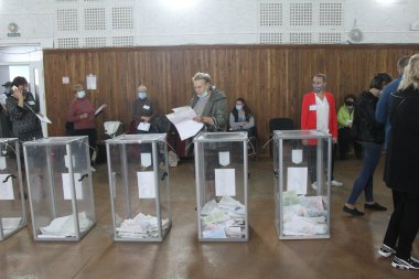 ODESSA, UKRAINE -25.10.2020 - Ukrayna 'da seçimler. COVID-19 Coronavirus salgını sırasında yerel meclis üyelerinin seçim platformu. Oy pusulalarıyla maske ve eldiven takan insanlar
