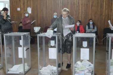 ODESSA, UKRAINE -25.10.2020 - Ukrayna 'da seçimler. COVID-19 Coronavirus salgını sırasında yerel meclis üyelerinin seçim platformu. Oy pusulalarıyla maske ve eldiven takan insanlar