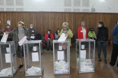 ODESSA, UKRAINE -25.10.2020 - Ukrayna 'da seçimler. COVID-19 Coronavirus salgını sırasında yerel meclis üyelerinin seçim platformu. Oy pusulalarıyla maske ve eldiven takan insanlar