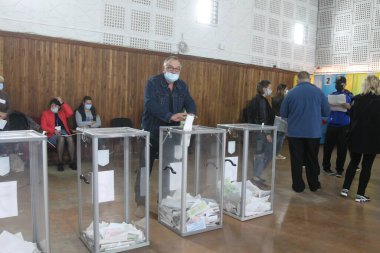 ODESSA, UKRAINE -25.10.2020 - Ukrayna 'da seçimler. COVID-19 Coronavirus salgını sırasında yerel meclis üyelerinin seçim platformu. Oy pusulalarıyla maske ve eldiven takan insanlar