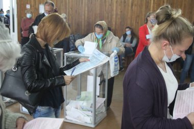 ODESSA, UKRAINE -25.10.2020 - Ukrayna 'da seçimler. COVID-19 Coronavirus salgını sırasında yerel meclis üyelerinin seçim platformu. Oy pusulalarıyla maske ve eldiven takan insanlar