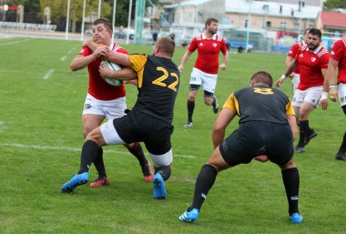 ODESSA, UKRAINE -20.10.17 - Ukrayna ragbi şampiyonası finali CREDO (Odessa) - kırmızı, OLYMPIK (Kharkiv) siyah rugby oyuncularının top için yoğun mücadelesi. Yeşil sahada dinamik bir oyun. Acımasız ragbi