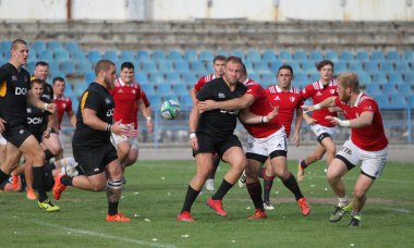 ODESSA, UKRAINE -20.10.17 - Ukrayna ragbi şampiyonası finali CREDO (Odessa) - kırmızı, OLYMPIK (Kharkiv) siyah rugby oyuncularının top için yoğun mücadelesi. Yeşil sahada dinamik bir oyun. Acımasız ragbi